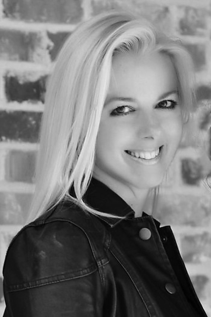 Black-and-white portrait of Tammy Kling smiling in front of a brick wall.